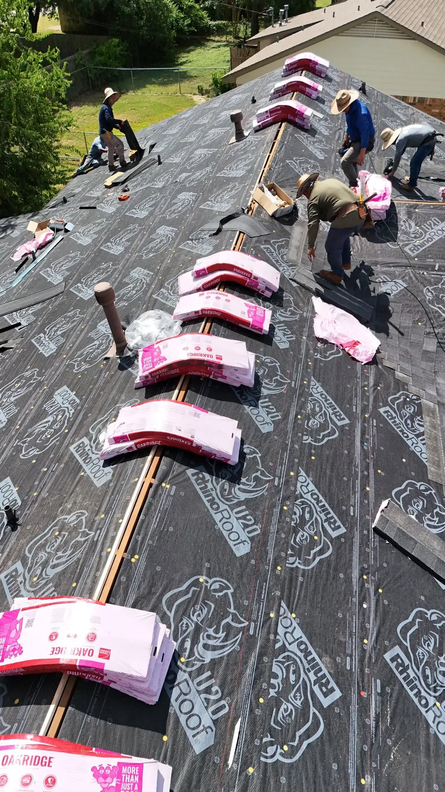 Roofers at work beside shingle bundles staged along the ridge