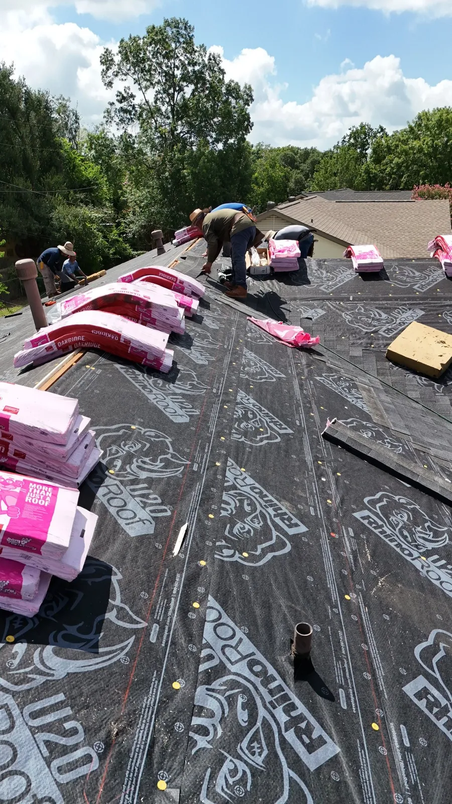 Shingle bundles stacked on fresh underlayment while roofers work